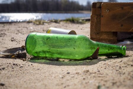 Old discarded empty green bottle and tin can lying in the shoreline of a lake conceptual of household pollutionの写真素材