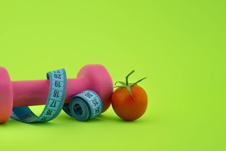 Still life with dumbbell, measuring tape and cherry tomato, as a concept of healthy nutrition and sports diet in close-up on green background and free copy spaceの写真素材