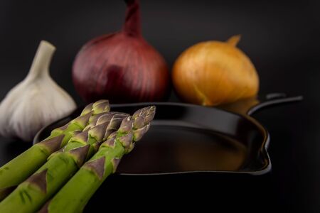 Skillet with fresh raw green spring asparagus spears and assorted red and white onions with garlic bulb ready for cookingの写真素材