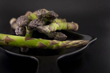 Skillet with fresh raw green spring asparagus spears ready for cooking over a black background with copy spaceの写真素材