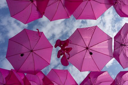 Street art installation of colorful bright pink umbrellas suspended against a cloudy skyの写真素材
