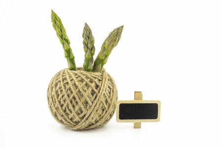 Fresh green asparagus spears and ball of natural hemp twine alongside a small slate or signboard isolated on white background, selective focus in a low angle viewの写真素材