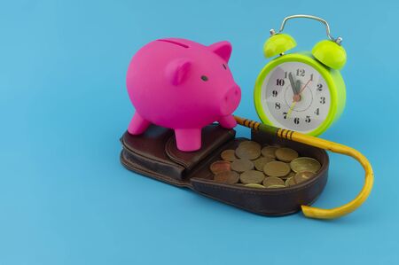 Saving for old-age and retirement concept with open purse with coins, walking stick, alarm clock and piggy bank over a blue background with copy spaceの写真素材