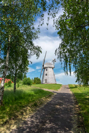 Picturesque empty country road leading to an old tower mill in rural area. Countryside landscape shot from low angle against blue skyの写真素材