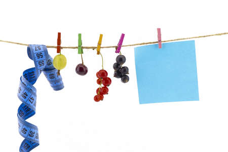 Fresh fruit, tape measure and blank sticky note hanging from clothes pegs on a rope with a gooseberry, red currants, cherry and black currants in a healthy diet conceptの写真素材