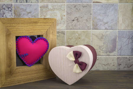 Handcrafted pink heart in a wooden frame with a heart shaped gift box against a tiled backgroundの写真素材