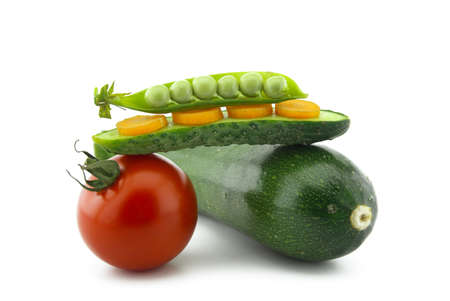 Healthy fresh vegetable still life over white with ripe red tomatoes, courgette or zucchini, carrots, peas in a pod and cucumber balance on top of each otherの写真素材