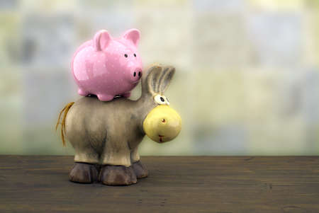 Cute little piggy bank and toy donkey close up side view against a blurred backgroundの写真素材