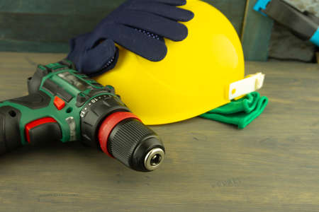 Cordless drill and yellow protective helmet and pairs of new blue gloves on a workbench, blurred in background. Construction tools and work equipment in close-up with copy spaceの写真素材