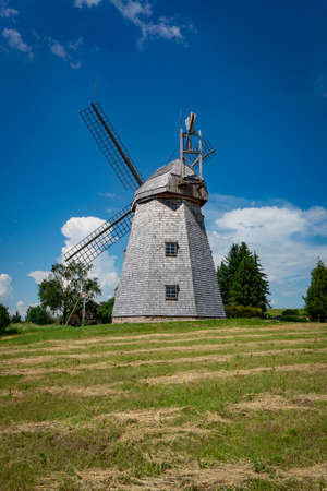 Old windmill in grassland in a country landscape with woodland trees under a cloudy blue sky in a scenic landscapeの写真素材