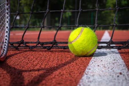 Shadows of racket and net surrounding a tennis ball on a white line on an outdoor court in sunshine in a sport and active lifestyle conceptの写真素材