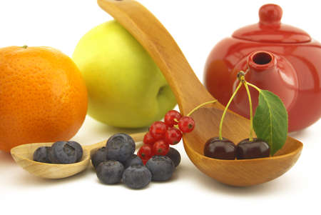 Fresh seasonal fruit still life with assorted berries including blueberries, cherries and red currants on wooden spoons with apple and orange and colorful red teapotの写真素材