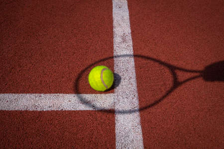 Shadows of net and racket surrounding a tennis ball on a white line on an outdoor court in sunshine in a sport and active lifestyle conceptの写真素材