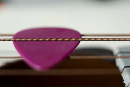 Colorful pink plectrum in guitar strings in a close up oblique angle view in a music and...
