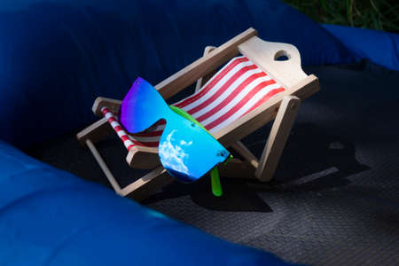 Sunglasses on a small striped deck chair balanced on a blue inflatable mattress in a concept of a summer vacationの写真素材