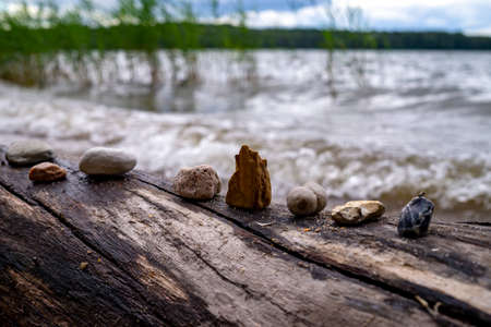 Row of stones and pebbles arranged on a log of driftwood on a beach at the edge of the sea in close...