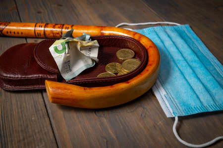 Conceptual Covid-19 flat lay still life with money spilling from an open purse onto a wooden table with cane and surgical mask alongside viewed from aboveの写真素材