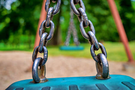 Close up detail of the chain attached to the seat on a playground swing in a low angle viewの写真素材