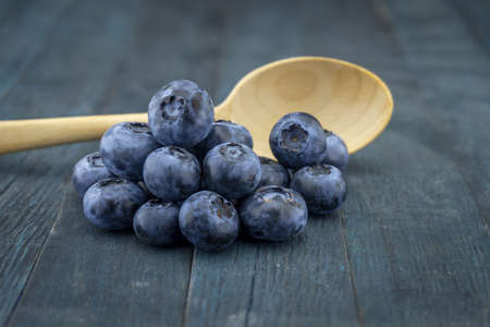 Bunch of fresh blueberries and wooden spoon on blue rustic board, low angle selective focus and free copy space for textの写真素材