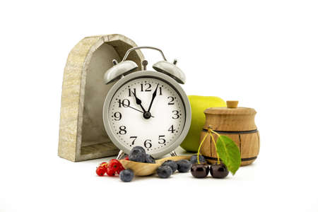 Culinary still life with old-fashioned alarm clock, apple, jar of honey, cherries, red currants and blueberries over white background with copy spaceの写真素材