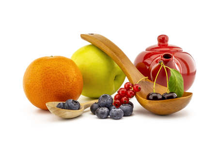 Fresh seasonal fruit still life with assorted berries including blueberries, cherries and red currants on wooden spoons with apple and orange and colorful red teapotの写真素材