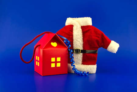 House shaped gift box with yellow glowing windows and red Santa Claus suit on a blue background. New Year and Christmas holiday season concept card decorationの写真素材