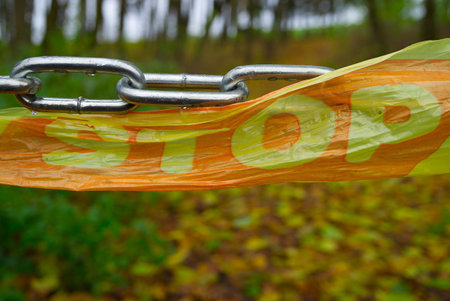 Close-up on chain barrier with stop sign on plastic tape in the woods. End of road or private property conceptの写真素材