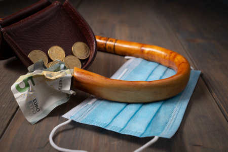 Money spilling from an open purse onto a wooden table with cane and surgical mask alongside viewed from above, old age and pandemic conceptual flat lay still lifeの写真素材