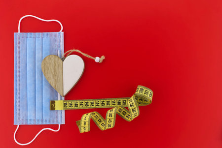 Social Distancing concept - wooden heart medallion of two separate sides placed on medical face mask...