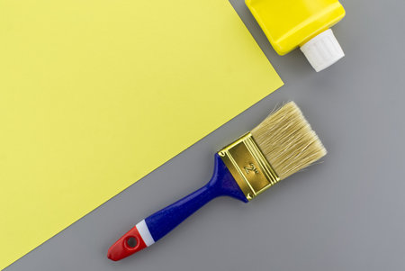 Renovation and color trends concept with clean paintbrush and pigment bottle on a two tone grey and yellow background with copy space viewed as a flat lay.の写真素材