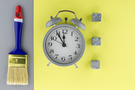 Conceptual image of alarm clock and new clean paintbrush on a two tone grey and yellow background with copyspace viewed as a flat lay still lifeの写真素材