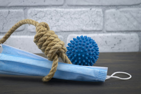Rope noose around a protective surgical face mask and virus molecule conceptual of death or mortality during the global Covid-19 or coronavirus pandemic against a brick wall backgroundの写真素材