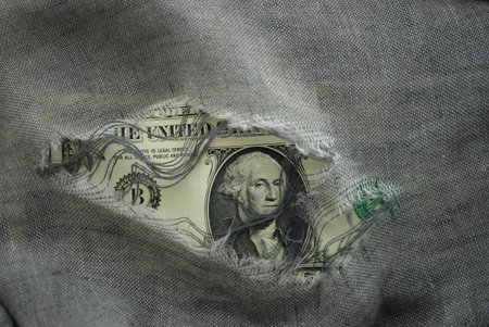 USD banknote viewed through a hole in torn grey fabric with focus to the portrait of Washington in a financial or economic conceptの写真素材
