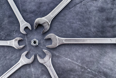 Circle of spanners or wrenches surrounding a nut on a grunge stone surface, top view