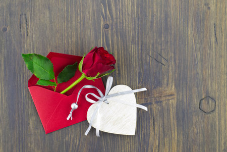 Red rose in envelope and heart medallion on wooden background with free copy space. Wishes, greetings and love messageの写真素材