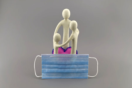 family concept with a small figurine of parents and a child embracing with pink heart and protective surgical face mask.の写真素材