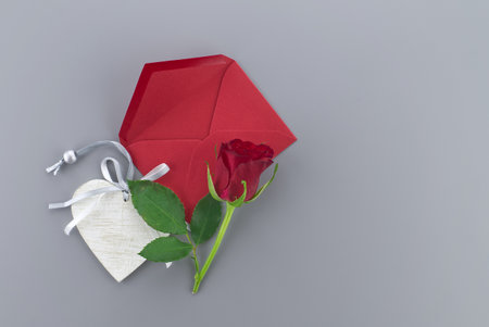 Red rose and wooden heart medallion above the envelope on gray background with free copy space. Wishes, greetings and love messageの写真素材