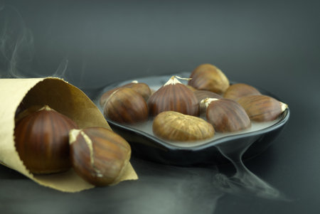 Roasting chestnuts in a black pan, surrounded by white smoke and a cone-shaped paper cone, a dish for a traditional healthy winter snack or appetizerの写真素材