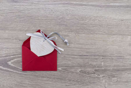 A heart-shaped wooden medallion is placed in a red envelope. Greetings and love letterの写真素材
