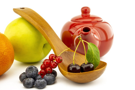 Fresh seasonal fruit still life with assorted berries including blueberries, cherries and red currants on wooden spoons with apple and orange and colorful red teapotの写真素材