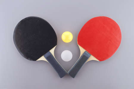 Red and black table tennis racks with a white and an yellow  ball on grey backgroundの写真素材