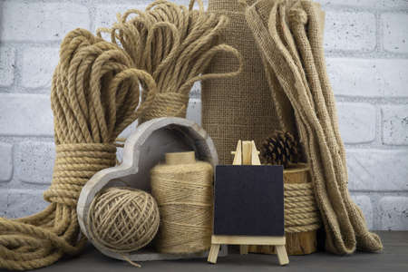 Assorted balls of hemp twine and string with skeins of rope, sackcloth fabric and slate chalkboard in a close up rustic still lifeの写真素材