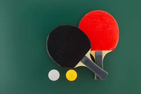 Two table tennis racks with a white and an yellow ball on green background with free copy spaceの写真素材