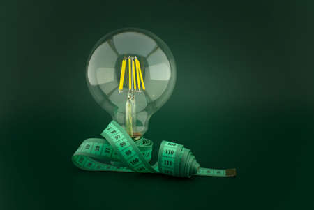 Slimming idea concept with lamp light bulb and measuring tape over a dark green backgroundの写真素材