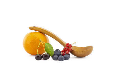 Fresh seasonal berries including blueberries, cherries and red currants, wooden spoon and orange on a white background with copy spaceの写真素材