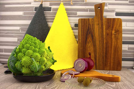 Salad preparation. Cauliflower romanesco, red onion and olives prepared for salads on the kitchen table, against the background of multicolored clothsの写真素材