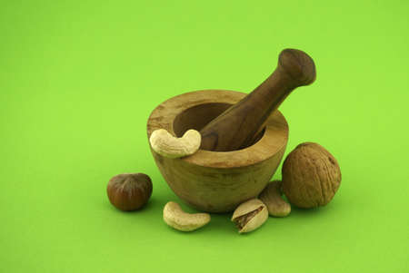 Wooden rustic-style mortar and pestle and various nuts over green background with free space for...
