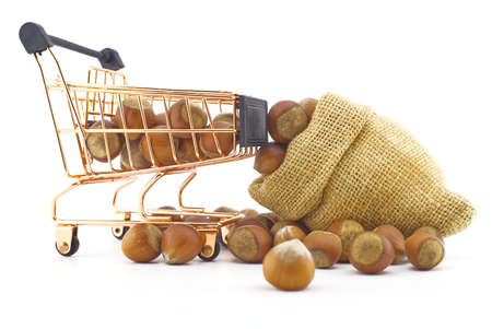 Shopping cart and small hessian bag filled with whole ripe hazelnuts spilling onto a white backgroundの写真素材