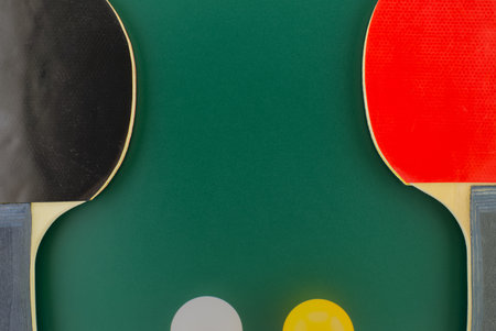 Red and black table tennis racks with a white and an yellow ball on green background with free copy spaceの写真素材