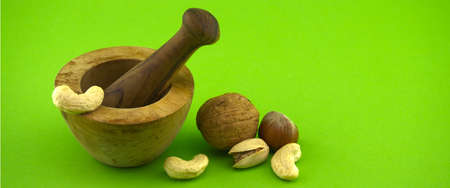 Wooden rustic-style mortar and pestle and various nuts over green background with free space for text. Spices and herb grinderの写真素材